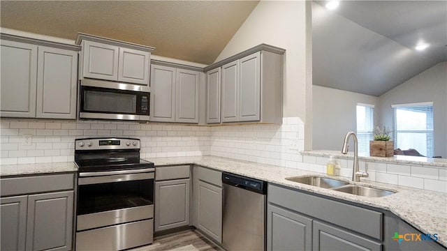 kitchen with vaulted ceiling, tasteful backsplash, sink, gray cabinetry, and stainless steel appliances