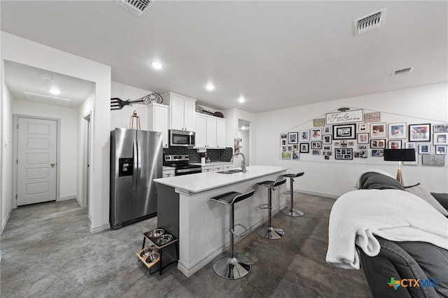 kitchen featuring appliances with stainless steel finishes, sink, white cabinets, a kitchen breakfast bar, and a center island with sink