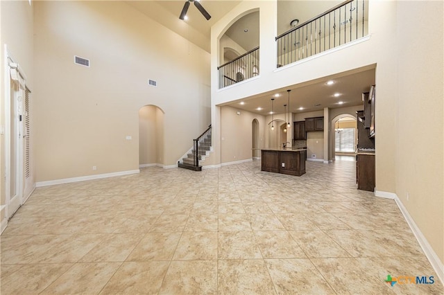 26815 Tulip Mdw, Boerne, TX 78015 - unfurnished living room featuring arched walkways, a high ceiling, a ceiling fan, and stairs