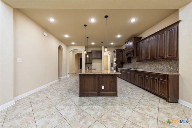 26815 Tulip Mdw, Boerne, TX 78015 - kitchen featuring arched walkways, light stone countertops, dark brown cabinetry, recessed lighting, and cooktop