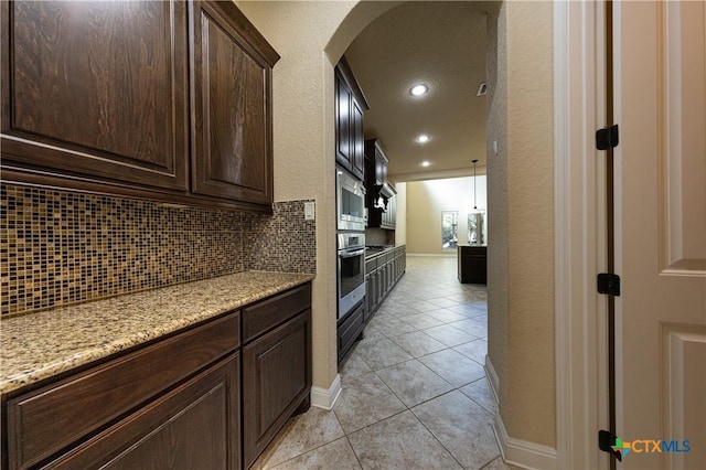 26815 Tulip Mdw, Boerne, TX 78015 - kitchen with arched walkways, backsplash, dark brown cabinets, stainless steel appliances, and light stone countertops