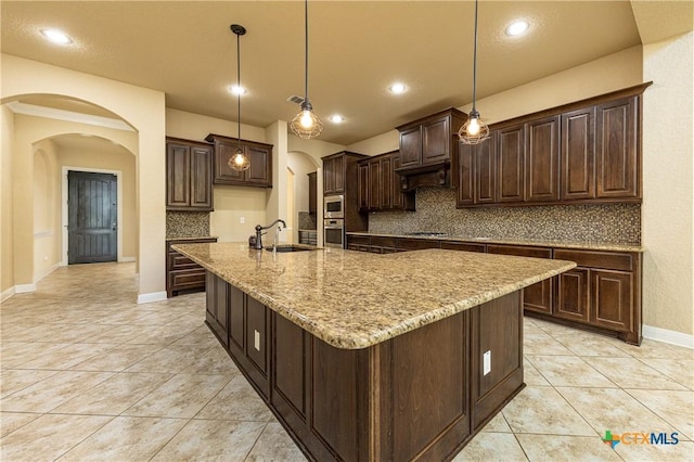 26815 Tulip Mdw, Boerne, TX 78015 - kitchen featuring arched walkways, tasteful backsplash, light stone counters, a spacious island, and light tile patterned flooring