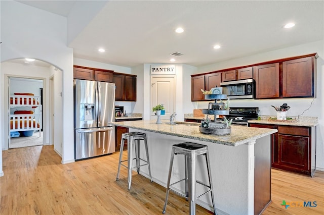 kitchen featuring stainless steel appliances, a center island with sink, light stone counters, a kitchen bar, and light hardwood / wood-style flooring