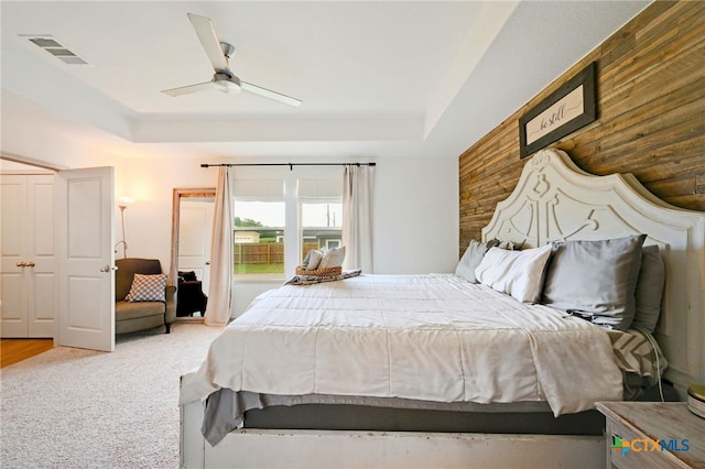 carpeted bedroom featuring wood walls, ceiling fan, and a tray ceiling