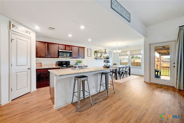 kitchen with light hardwood / wood-style floors, sink, a kitchen bar, an island with sink, and black range