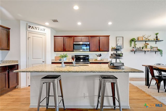 kitchen with a kitchen breakfast bar, a kitchen island with sink, black range, and light hardwood / wood-style flooring