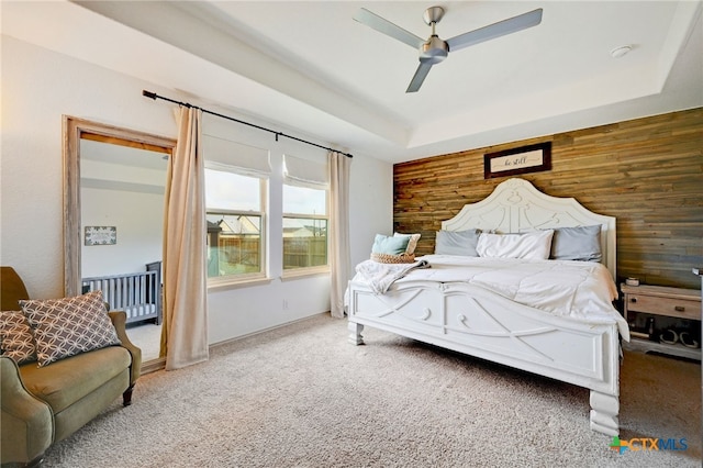 bedroom with wood walls, ceiling fan, carpet flooring, and a tray ceiling