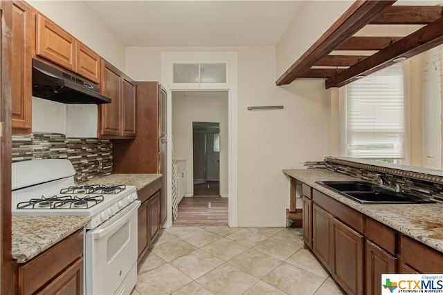 kitchen with light tile patterned floors, sink, white gas range oven, and light stone counters