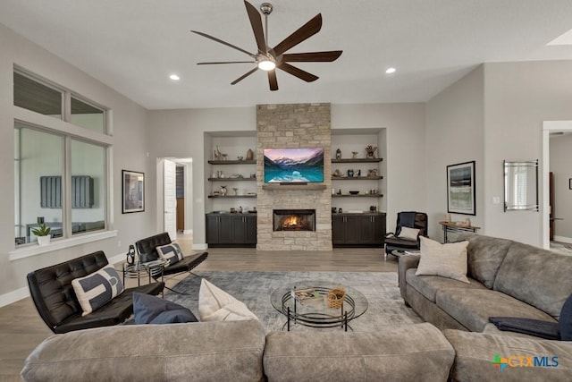 living room featuring built in shelves, recessed lighting, a large fireplace, wood finished floors, and baseboards