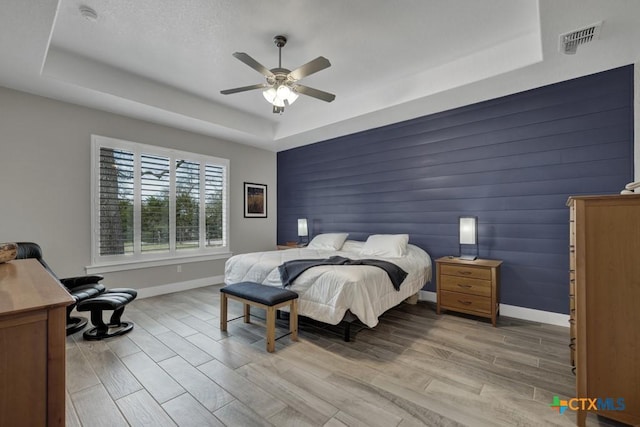 bedroom featuring light wood-type flooring, a raised ceiling, visible vents, and baseboards