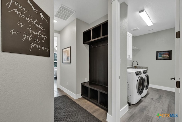 clothes washing area featuring light wood finished floors, washing machine and clothes dryer, visible vents, cabinet space, and baseboards