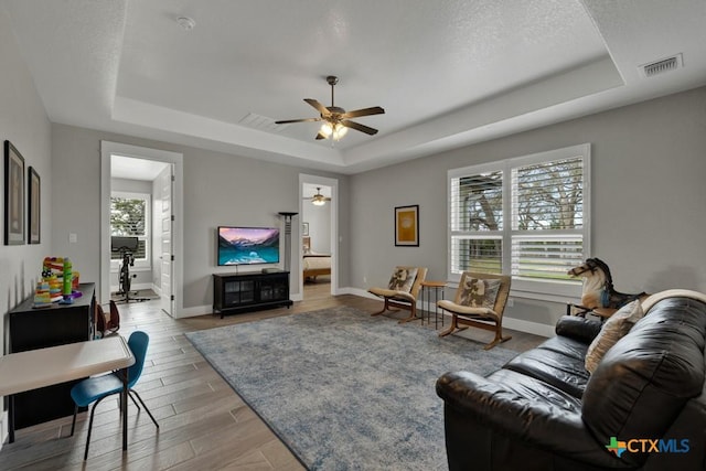 living room featuring visible vents, baseboards, a ceiling fan, light wood-style flooring, and a tray ceiling