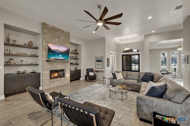 living room with visible vents, a stone fireplace, a textured ceiling, and light wood finished floors