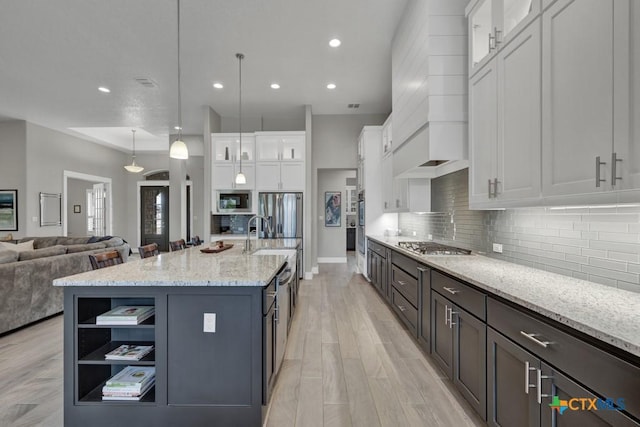 kitchen featuring a kitchen island with sink, white cabinets, appliances with stainless steel finishes, glass insert cabinets, and pendant lighting