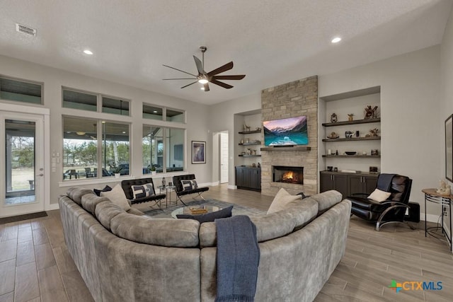 living room with a textured ceiling, built in shelves, a fireplace, visible vents, and wood tiled floor