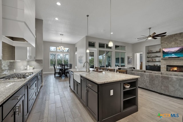 kitchen featuring a center island with sink, light stone countertops, stainless steel appliances, pendant lighting, and a sink