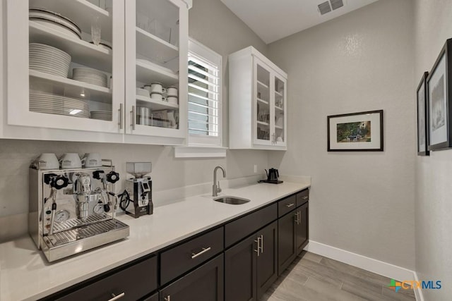 bar featuring visible vents, a sink, light wood finished floors, and baseboards