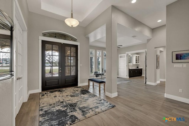 entrance foyer featuring a tray ceiling, french doors, a high ceiling, wood finished floors, and baseboards