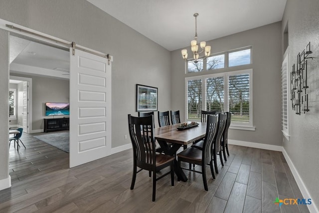 dining space featuring a chandelier, a barn door, wood finished floors, and baseboards