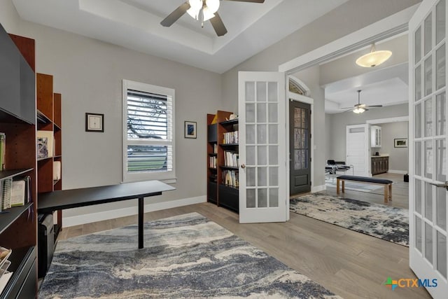 home office featuring ceiling fan, baseboards, french doors, a tray ceiling, and light wood finished floors