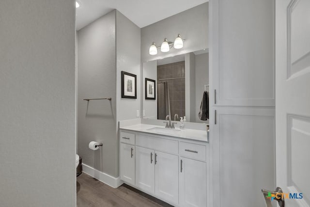 full bathroom featuring toilet, a tile shower, vanity, wood finished floors, and baseboards