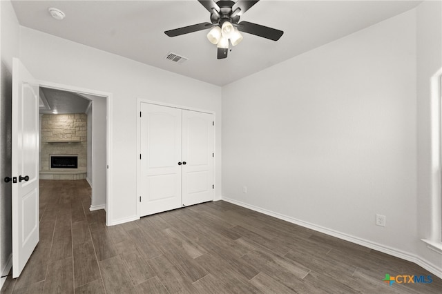 unfurnished bedroom featuring a stone fireplace, dark hardwood / wood-style floors, ceiling fan, and a closet