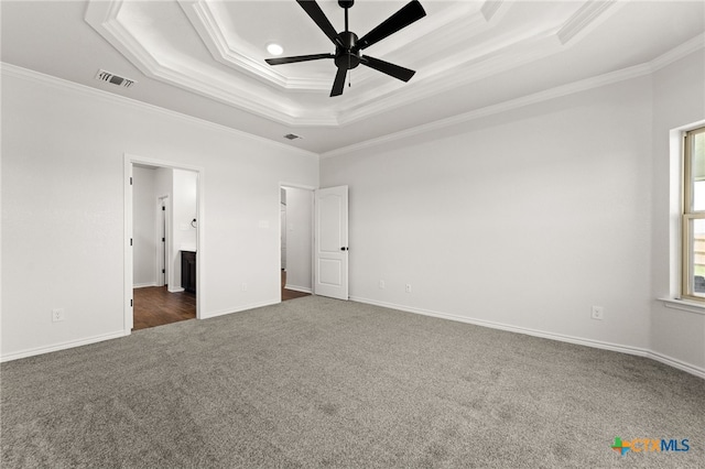 unfurnished bedroom with ceiling fan, a tray ceiling, dark colored carpet, and ornamental molding