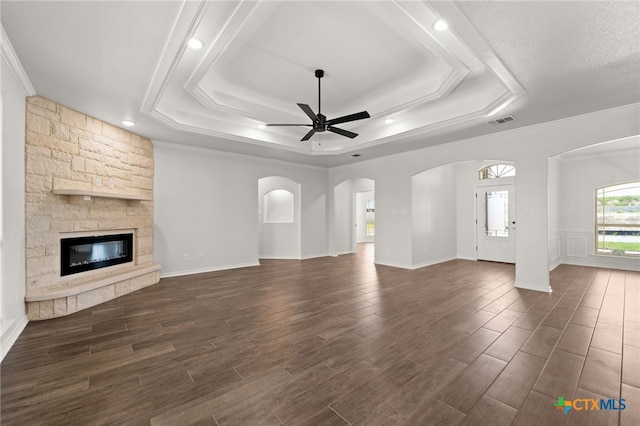 unfurnished living room with a stone fireplace, ceiling fan, dark hardwood / wood-style floors, and a raised ceiling