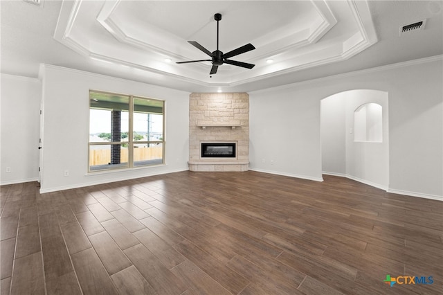 unfurnished living room with dark hardwood / wood-style flooring, a tray ceiling, ceiling fan, and a stone fireplace