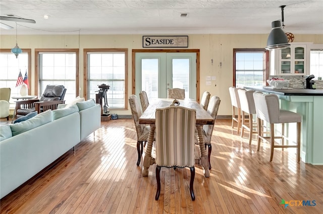 dining space featuring light hardwood / wood-style floors, a healthy amount of sunlight, a textured ceiling, and french doors