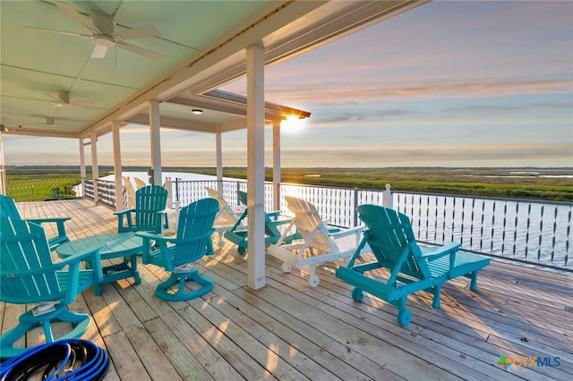 deck at dusk with a water view and ceiling fan