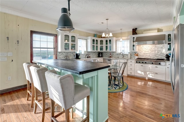 kitchen with light wood-type flooring, white cabinetry, hanging light fixtures, and stainless steel appliances