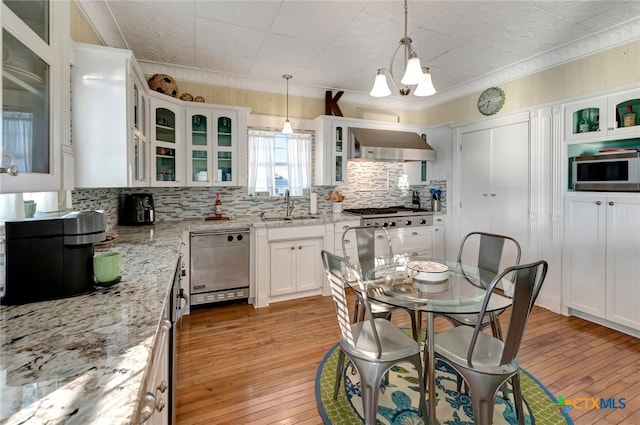 kitchen featuring light stone counters, stainless steel appliances, light wood-type flooring, wall chimney range hood, and pendant lighting