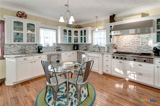 kitchen with light stone counters, backsplash, pendant lighting, sink, and light hardwood / wood-style flooring