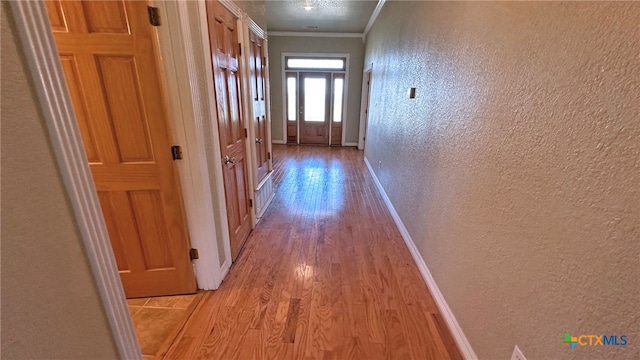 corridor with light hardwood / wood-style flooring and ornamental molding