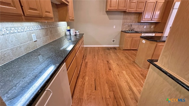 kitchen with light hardwood / wood-style flooring, sink, dark stone countertops, and backsplash