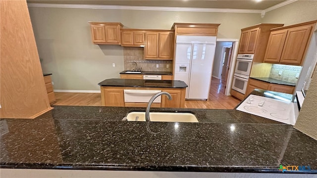 kitchen with ornamental molding, dark stone counters, sink, light hardwood / wood-style floors, and white appliances