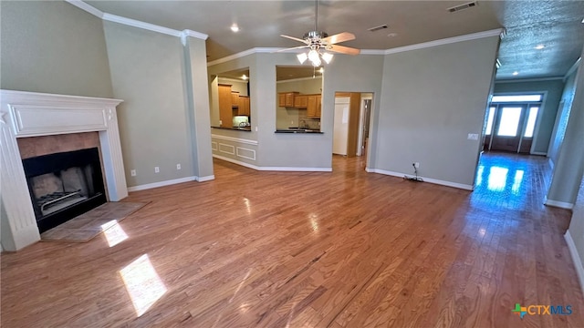 unfurnished living room featuring ornamental molding, light hardwood / wood-style flooring, ceiling fan, and a tiled fireplace