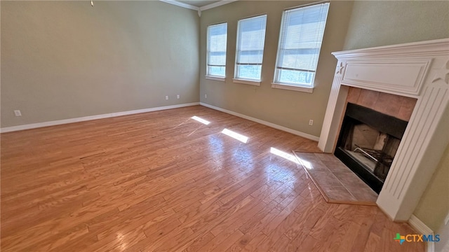 unfurnished living room featuring a tiled fireplace, light wood-type flooring, and crown molding