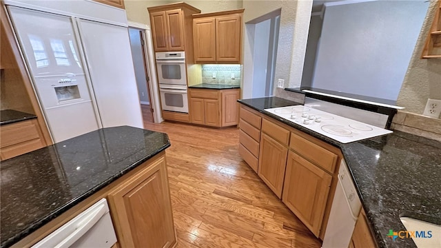 kitchen featuring white appliances, light hardwood / wood-style floors, and dark stone counters