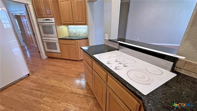 kitchen featuring white appliances, light hardwood / wood-style floors, and dark stone countertops