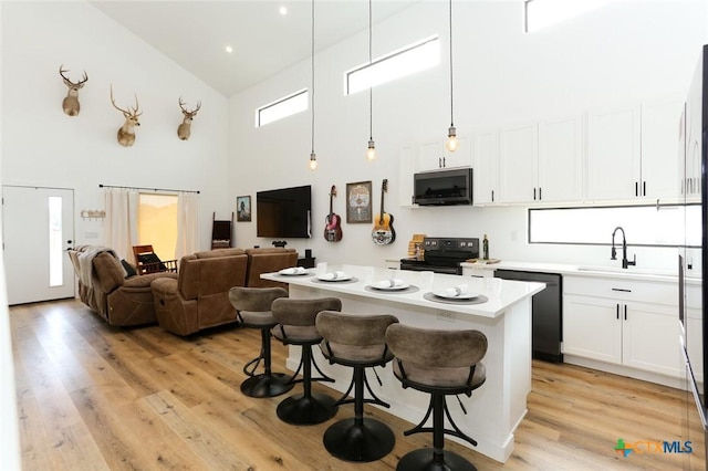 kitchen featuring high vaulted ceiling, pendant lighting, a kitchen bar, white cabinets, and black appliances