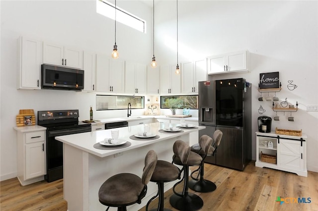 kitchen featuring a kitchen bar, black appliances, light hardwood / wood-style flooring, white cabinets, and a kitchen island