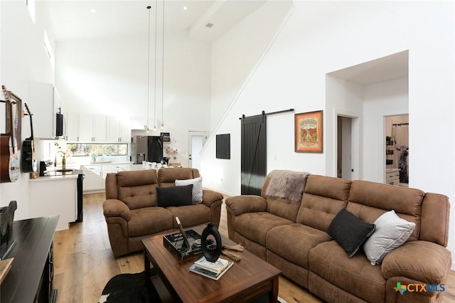 living room featuring a barn door, light wood-type flooring, a towering ceiling, and sink