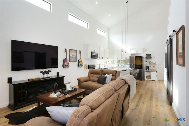 living room featuring a barn door, light wood-type flooring, and a towering ceiling