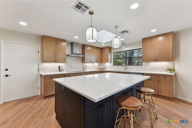kitchen with wall chimney range hood, light wood finished floors, visible vents, and a center island
