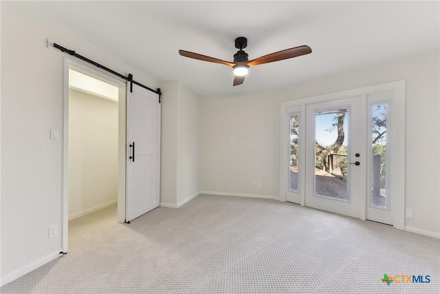 interior space featuring light colored carpet, ceiling fan, a barn door, and baseboards