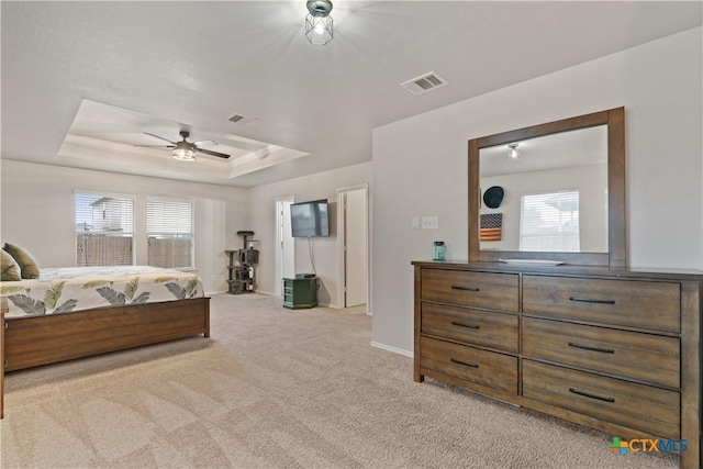 carpeted bedroom featuring multiple windows, ceiling fan, and a tray ceiling