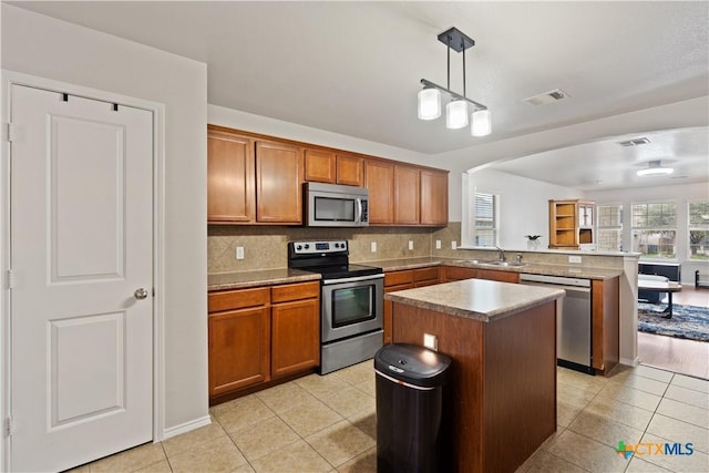 kitchen with sink, appliances with stainless steel finishes, decorative backsplash, a kitchen island, and decorative light fixtures