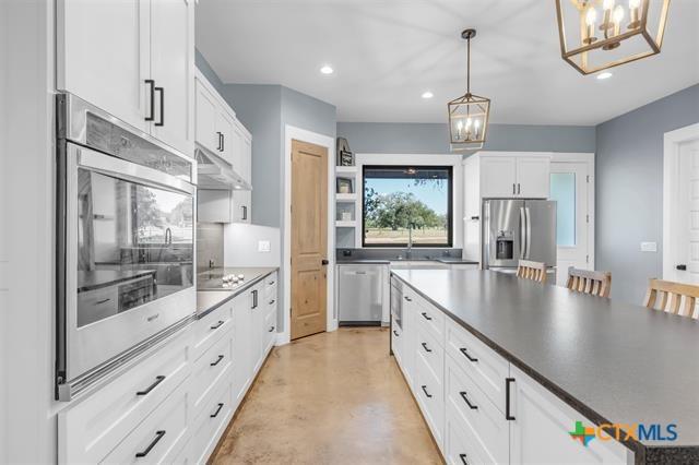 kitchen with appliances with stainless steel finishes, an inviting chandelier, white cabinetry, and pendant lighting